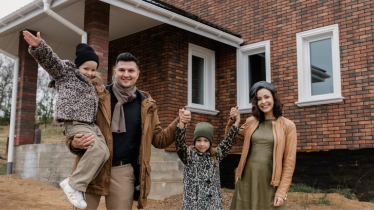 A happy family in front of their sturdy new home built with the best cement for construction.