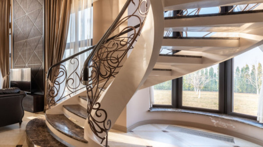 Types of stairs in building construction, showcasing a spiral staircase with intricate railings in a luxury home.