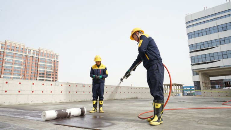 Workers applying waterproofing material on a concrete rooftop using modern waterproofing techniques.