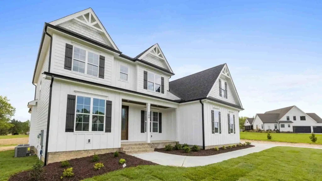 A beautiful white two-story house built with the best bricks for construction, surrounded by a lush green yard and a clear blue sky.